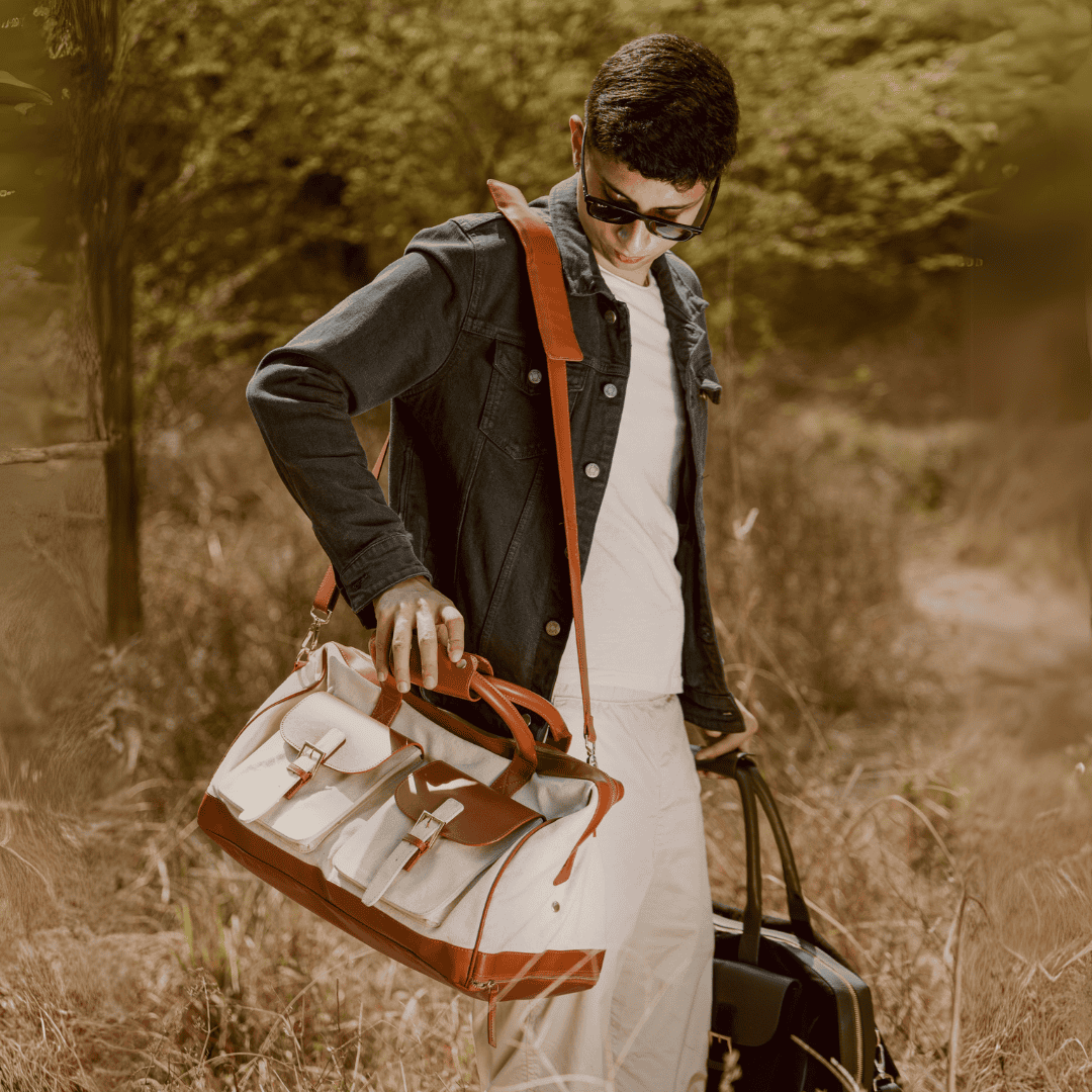 Person carrying Ajax plant leather duffle bag in beige and gingerbread colour during travel outdoors, styled as a weekend travel bag
