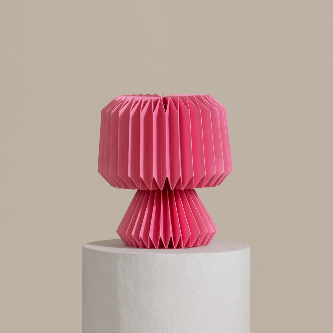 Pink folded paper lamp on a white pedestal against a beige background