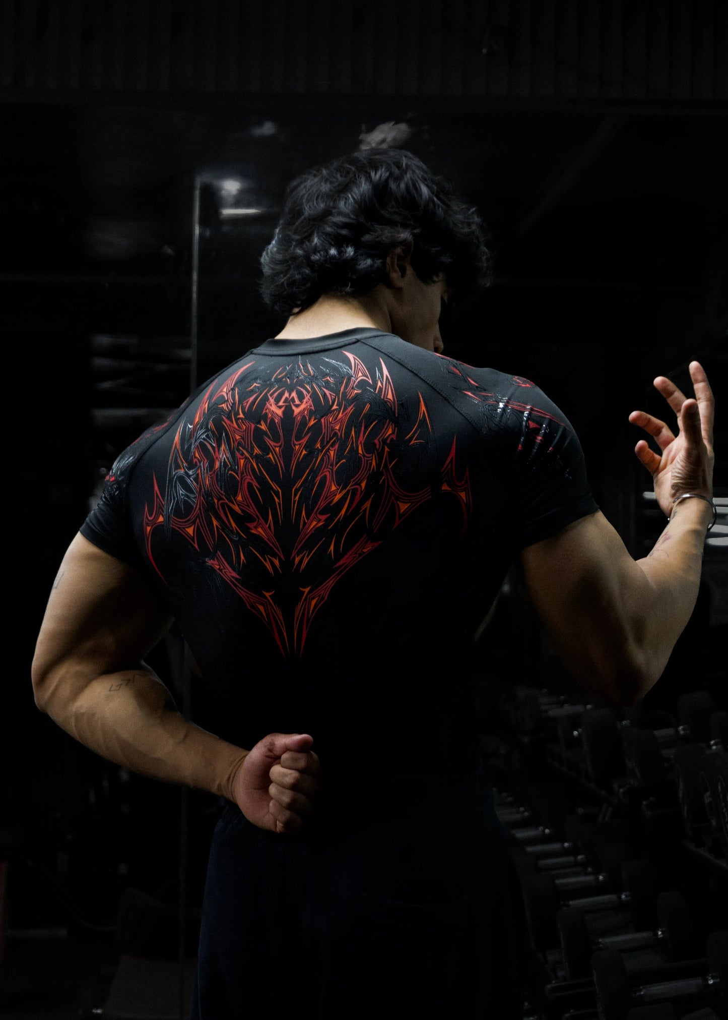 Person wearing a black t-shirt with red and white design, standing in a dark room.