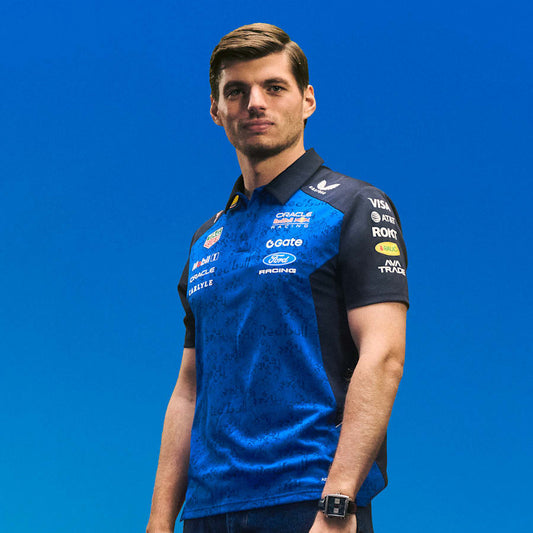 Max Verstappen wearing a blue and black polo shirt with various logos on a blue background
