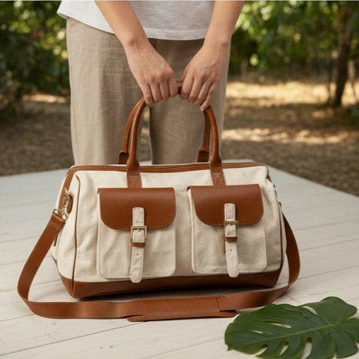 Ajax plant leather duffle bag in beige and gingerbread colour held by hand outdoors on a wooden surface, showcasing lifestyle use and spacious design