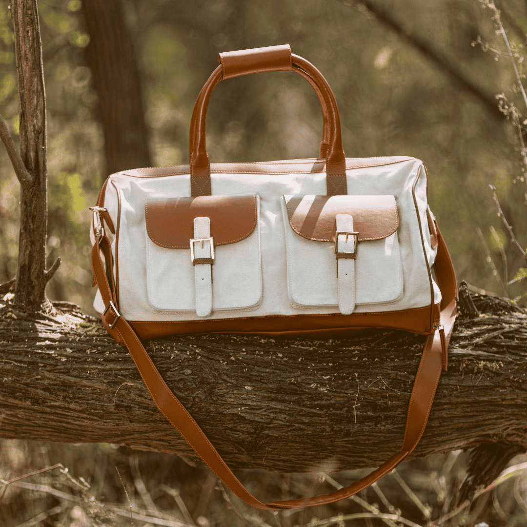 Ajax plant leather duffle bag in beige and gingerbread colour placed on a tree branch in a natural outdoor setting, highlighting travel durability and design