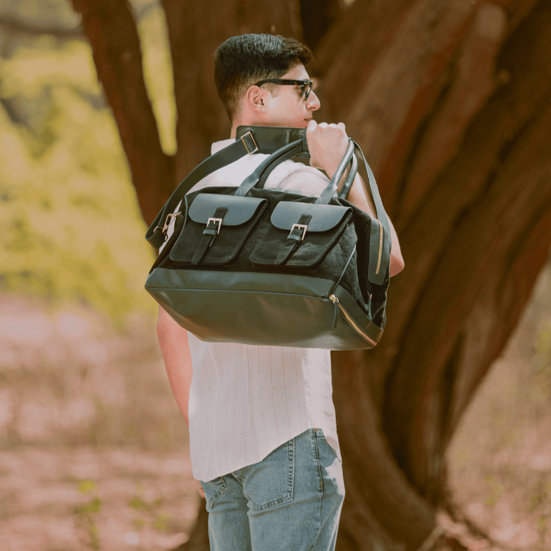 Person carrying Ajax plant leather duffle bag in black and forest green colour over shoulder outdoors, travel lifestyle view