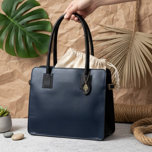 Navy blue and black plant leather tote bag held by hand against a natural textured background with foliage