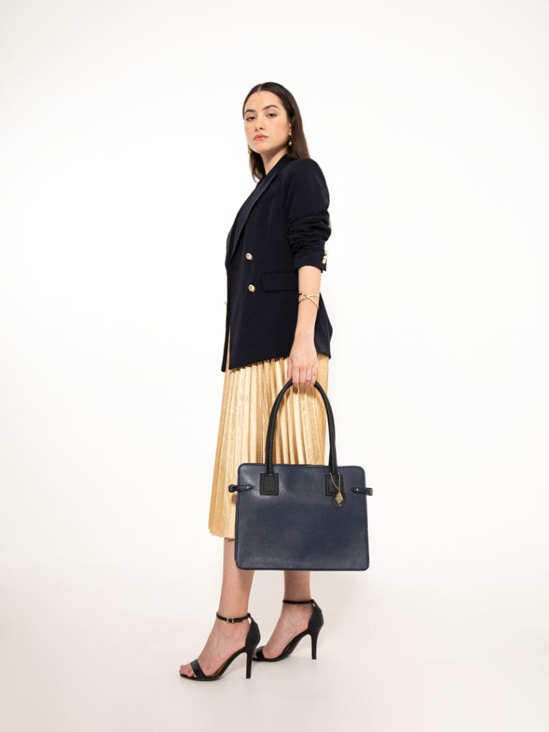 Woman carrying navy blue and black plant leather tote bag styled with formal outfit on a neutral background