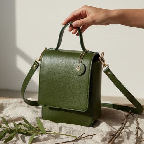 Ceres green plant leather crossbody bag held by hand showing structured design and adjustable strap on a light neutral background